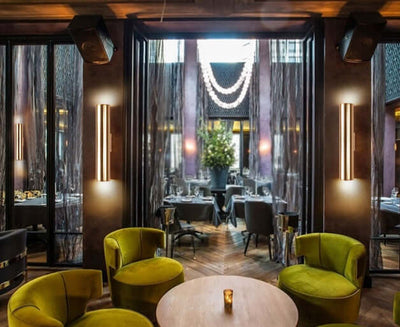 Stylish restaurant interior featuring green armchairs, elegant decor, and illuminated wall lamps creating a cozy atmosphere.