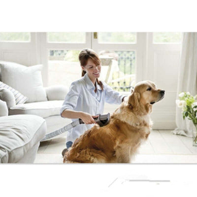 Woman using a vacuum attachment grooming tool on a golden retriever dog indoors.