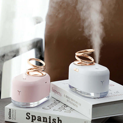 Suspended double ring mini humidifiers in pink and white, releasing mist, placed on coffee table with books.