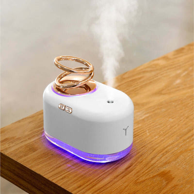 Suspended double ring humidifier on a wooden table, producing mist with a stylish design and LED illumination.