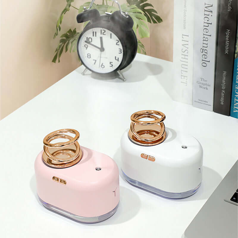 Suspended double ring humidifiers in pink and white on a desk with a clock, ideal for home use and water replenishment.