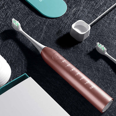 Sleek sonic electric toothbrush in rose gold with interchangeable brush heads on a dark textured background.