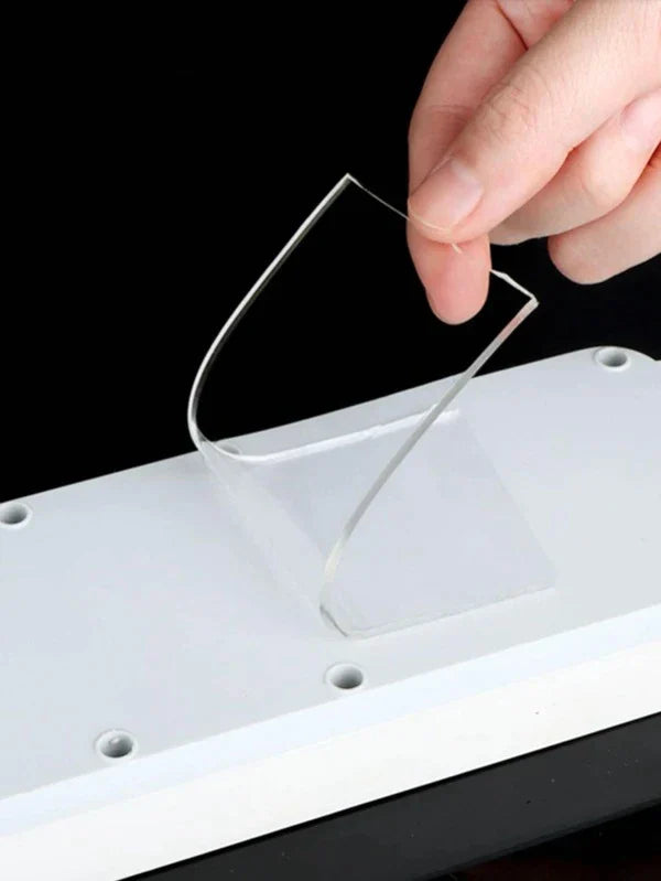 Hand peeling off a piece of double sided reusable tape from a surface, demonstrating its easy application.