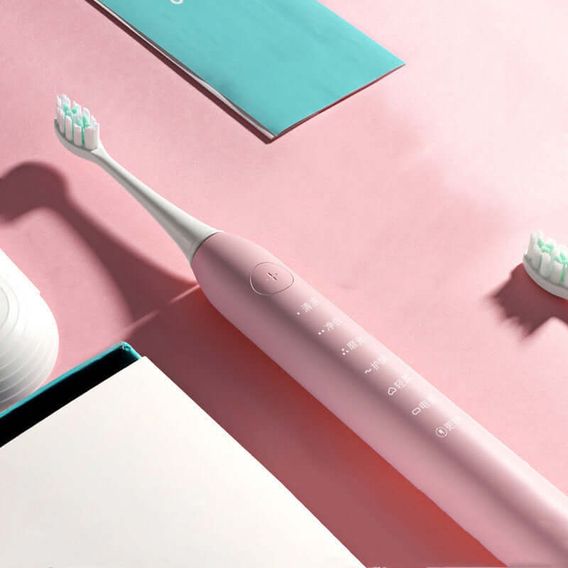 Pink electric toothbrush with multiple brushing modes and charging station on a pastel pink background.