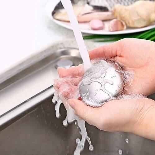 Hands using odour removing steel soap under running water in a kitchen sink.