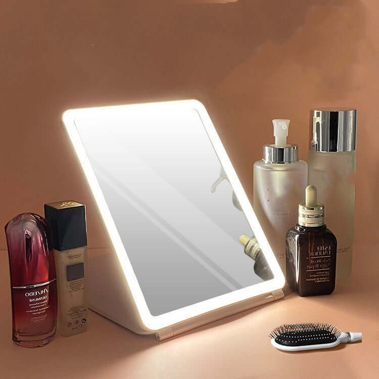 Clamshell desktop LED touch dressing mirror with light beside beauty products and a comb