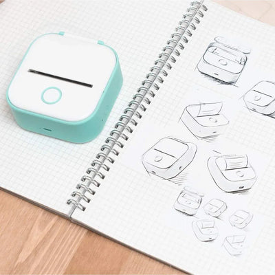 Portable printer next to sketches in a notebook, showcasing compact design and versatility for on-the-go printing.