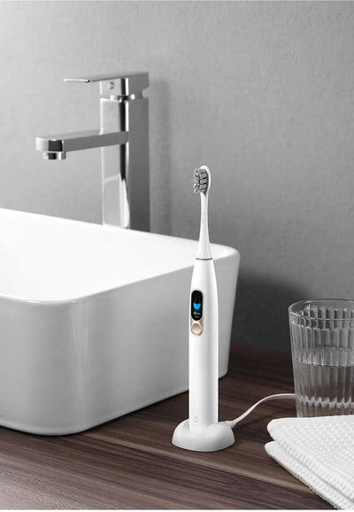 Electric toothbrush with charging base on bathroom countertop next to a sink, showcasing modern design and functionality.