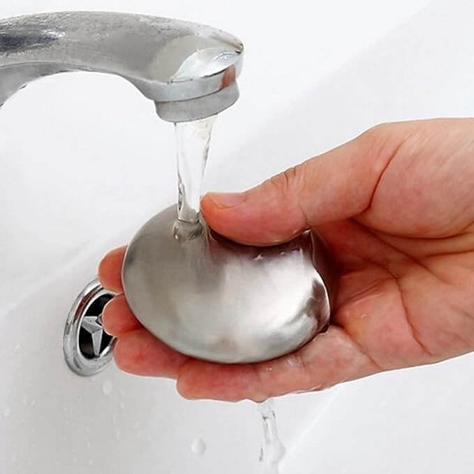 Person using odour removing steel soap under running water in the kitchen sink.