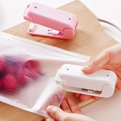 Mini heat sealer in use, sealing a food bag with fruits on a wooden cutting board.