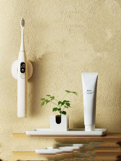 Sleek electric toothbrush on wall mount with toothpaste and a plant on a wooden shelf, showcasing modern bathroom aesthetics.