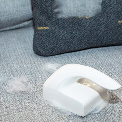 White pet hair remover on grey fabric couch, efficiently picking up cat hair and lint.