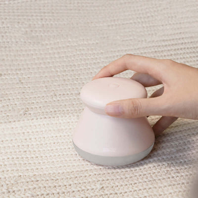 Rechargeable hair remover in pink color held by hand on textured fabric.
