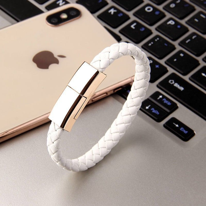 Stylish white charging bracelet with gold clasp resting beside a smartphone on a desk.