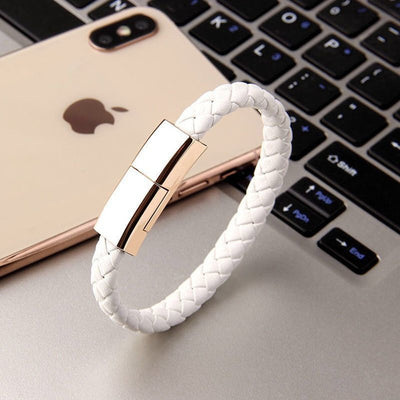 Stylish white charging bracelet with gold clasp resting beside a smartphone on a desk.