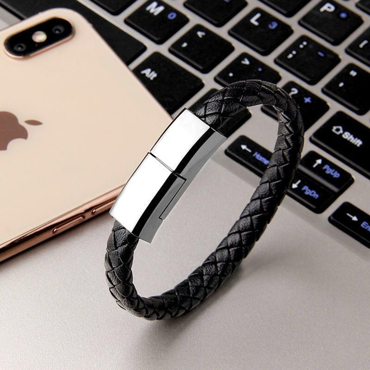 Stylish black braided charging bracelet next to a smartphone on a laptop keyboard.