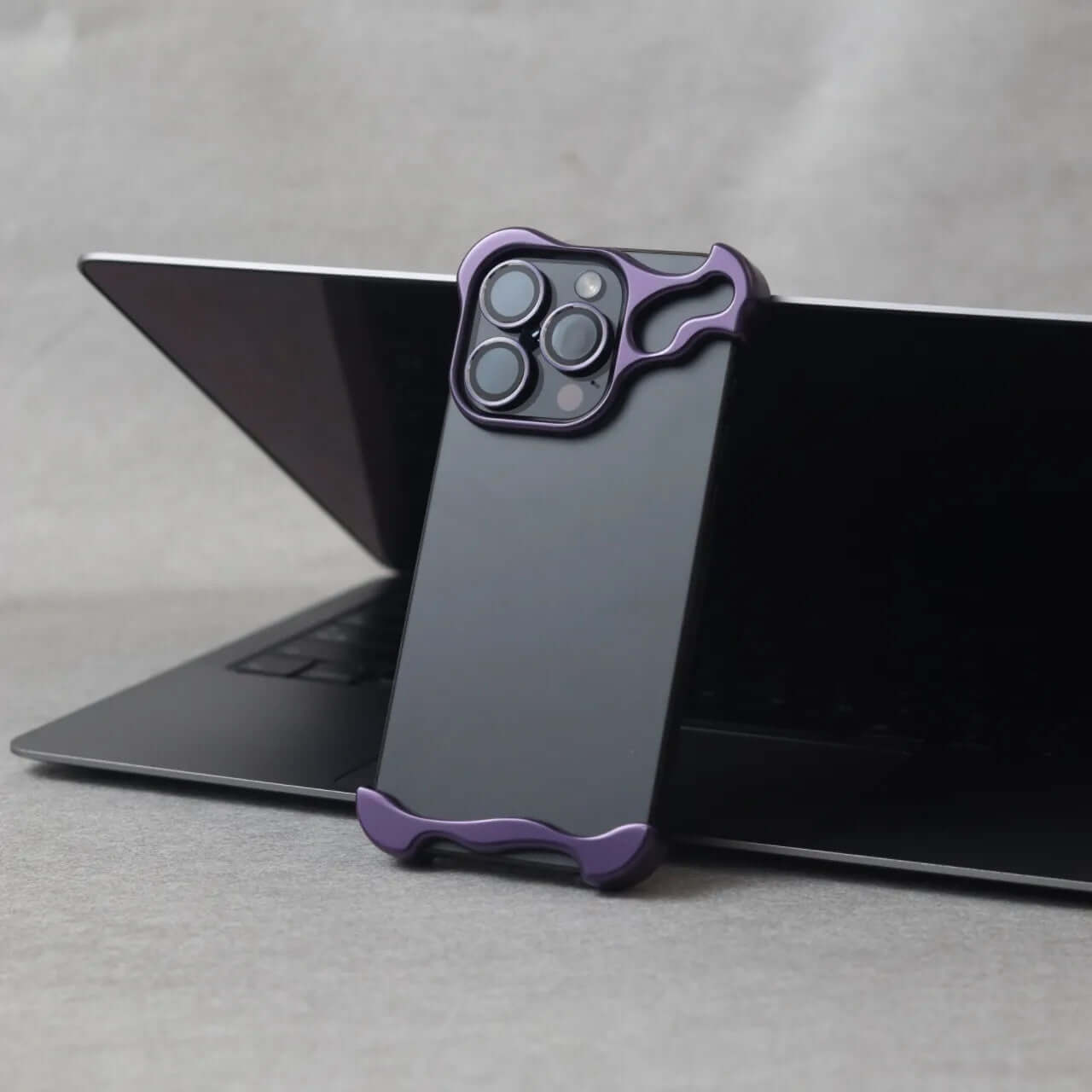 Zinc alloy protective phone case in dark purple on laptop, designed for iPhone 15 series with minimalist style.