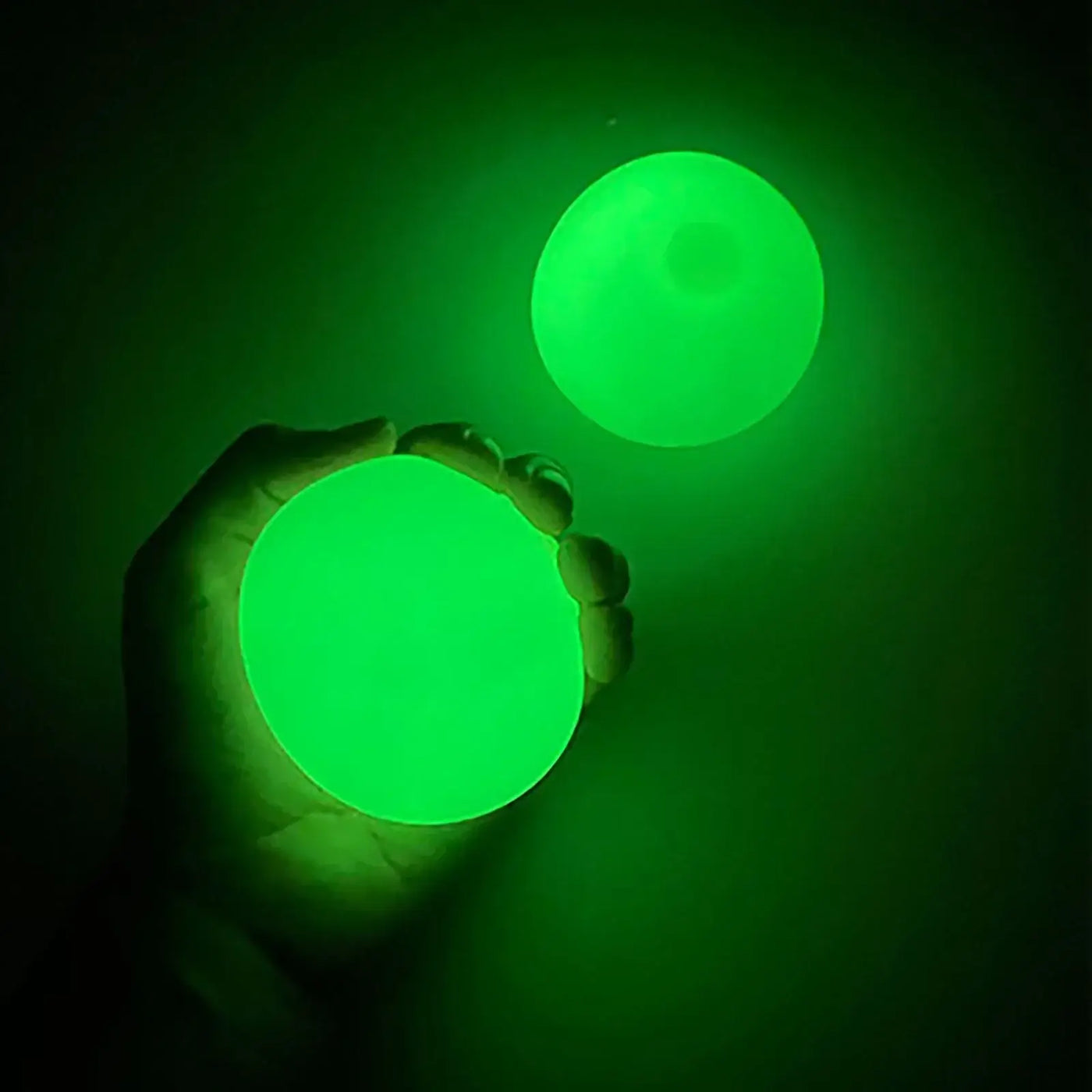 Person holding two glowing green sticky glow balls in a dark environment, showcasing their vibrant color.